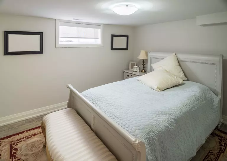 A bedroom in the basement of a home that is naturally lit by a single-hung window.