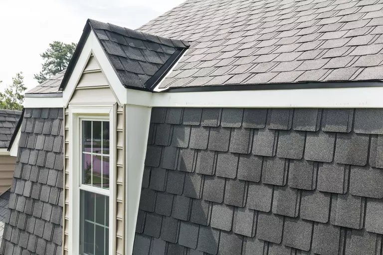 Gambrel-style roof featuring black shingles and a dormer with a window.