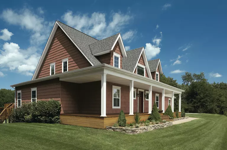 Exterior of a gable roof home with a porch and red vinyl siding.