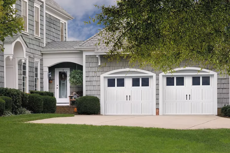 Pair of white carriage house-style garage doors on a home with a light gray exterior.