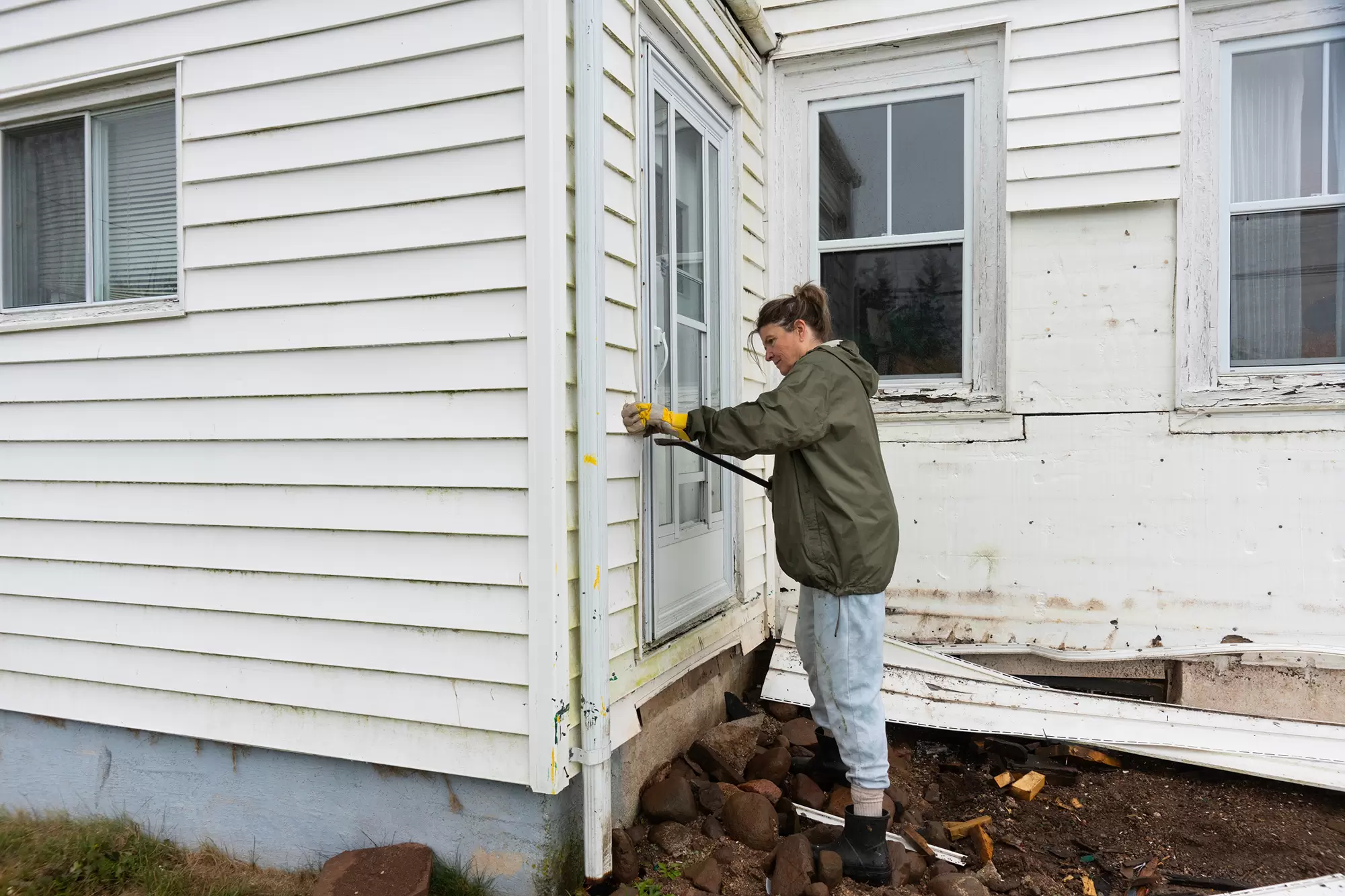 Person removing old siding from house exterior.