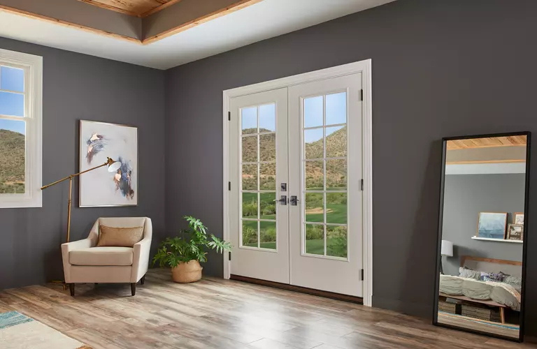 he master bedroom of a home, painted dark gray with neutral-toned furniture and a white hinged patio door leading to an open, large backyard space.