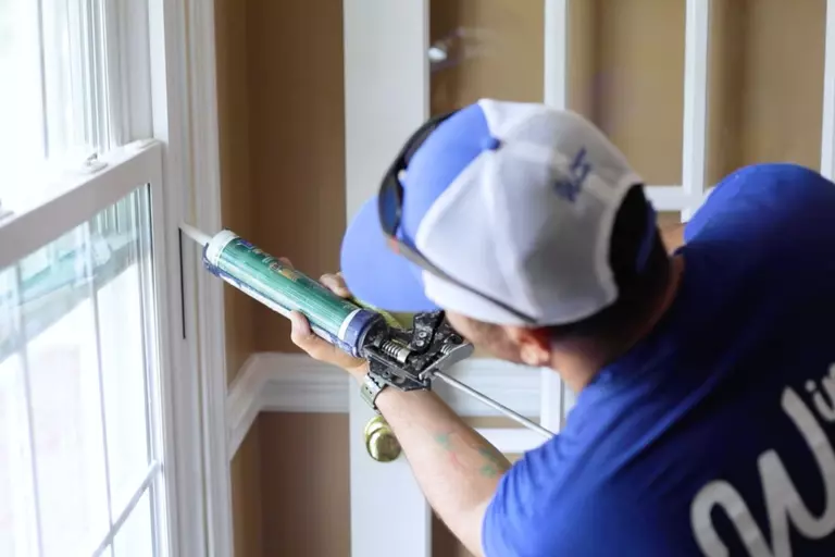 A Window World installer caulking the interior of a new window.