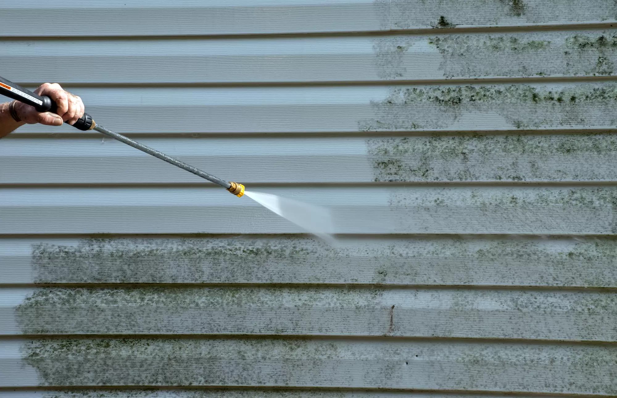 Pressure washing mold off vinyl house siding.