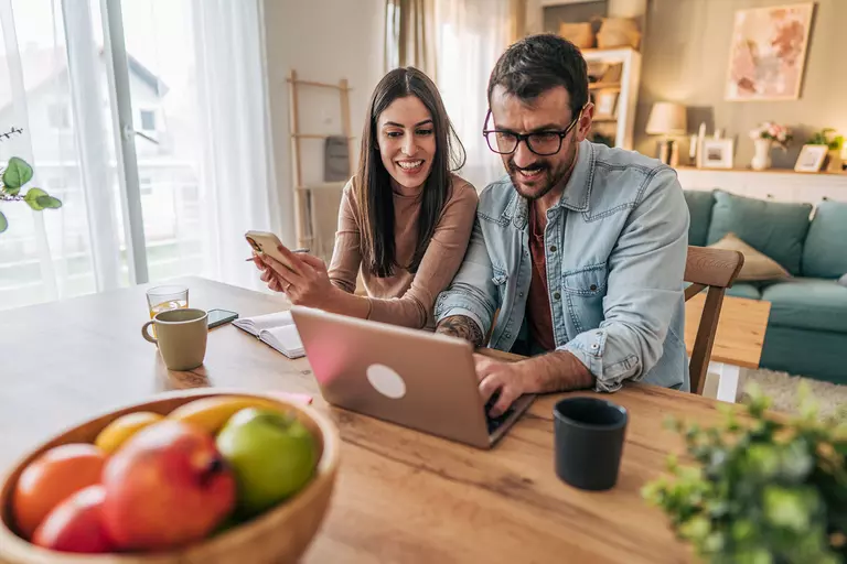 Man and woman smiling while using a laptop and smartphone.