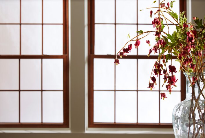 A pair of closed double-hung windows behind a floral arrangement in a vase. The windows need troubleshooting because they won’t stay up.