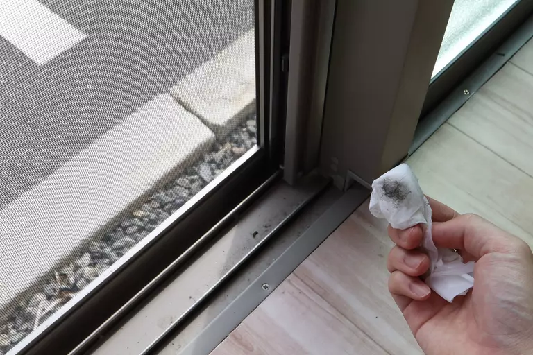 Close-up of a person’s hand wiping clean a patio door track.