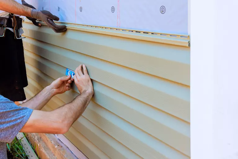 Workers measuring vinyl siding width on a house in a residential area.