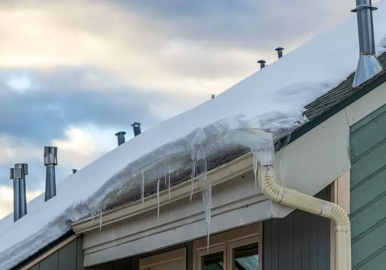 Heavy snow on the roof of a home leading to gunk, ice, and other debris in the gutters.