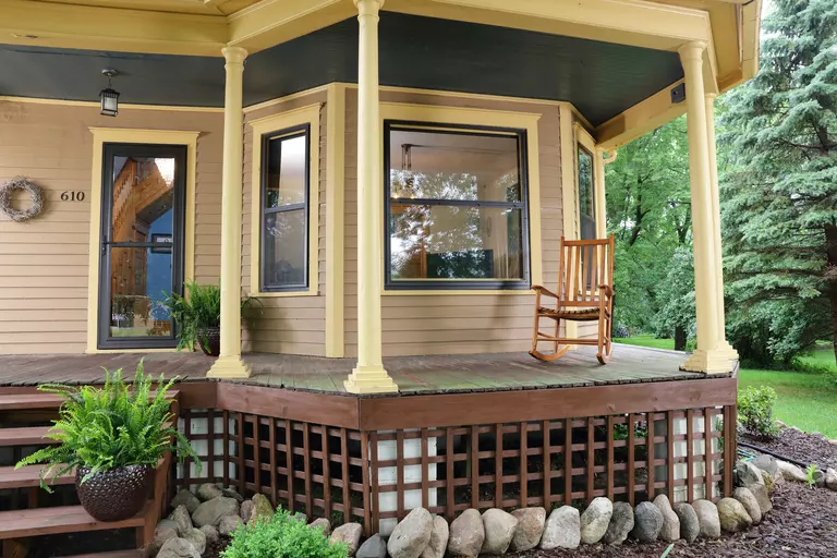 An energy-efficient storm door attached to the front of a home with a spacious front porch and brown columns around a rocking chair.