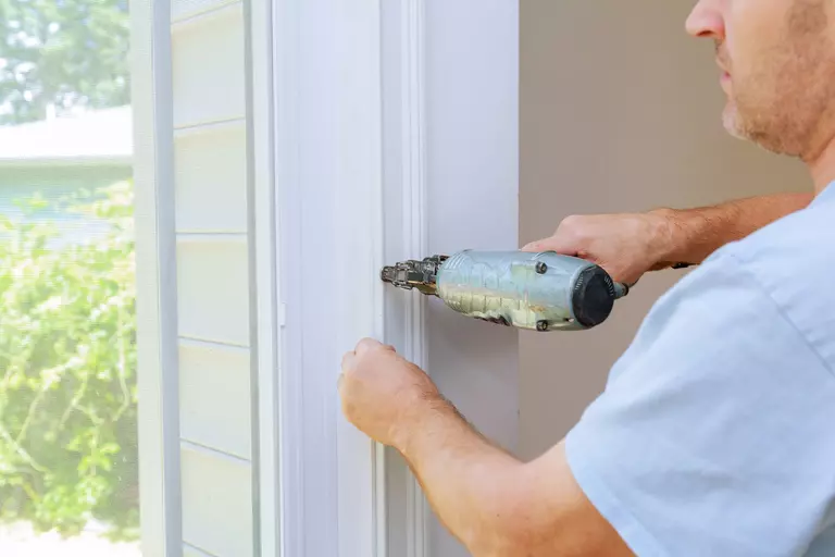 Close-up of a man using an air gun for nailing while performing exterior door installation on a home