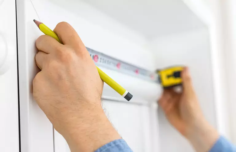 Person holding up tape measure against an exterior door with a pencil in one hand 