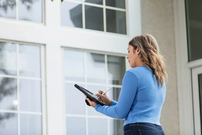 A woman taking notes on a tablet while inspecting a home’s windows.