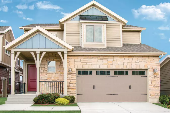 Taupe colored vertical short panel garage door with stockbridge windows and decorative hardware on a two-story home