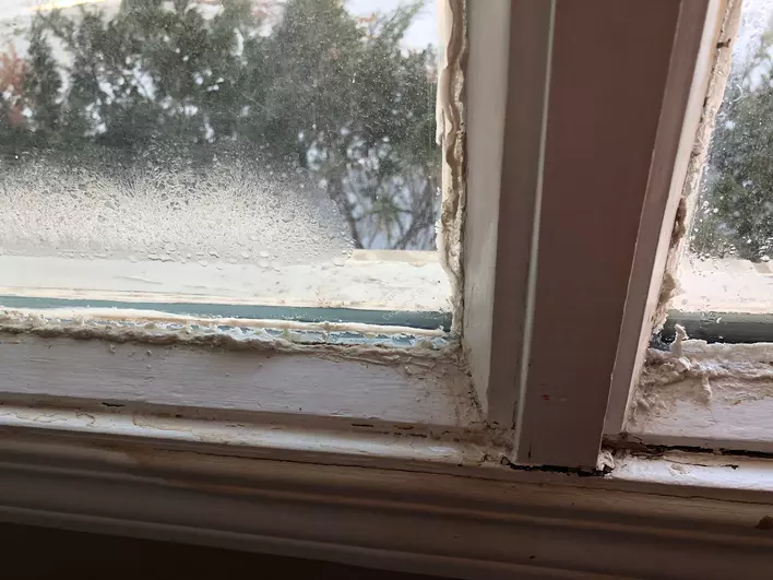 An old window with a warped frame, letting in a draft and causing condensation.