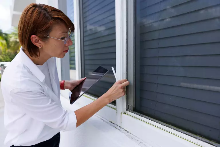 A woman inspecting a window on the exterior of a home.