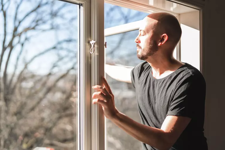 A man opening a large casement window.