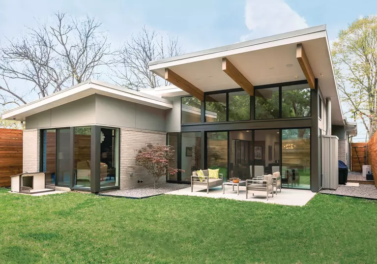 A modern home with large window on the backside of the home that lead out to a spacious and decorated outdoor living space.