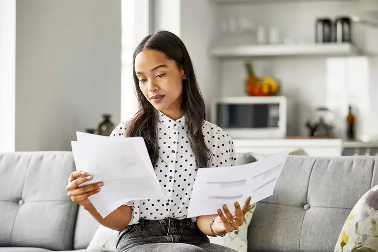 Woman comparing two sets of documents on a couch.