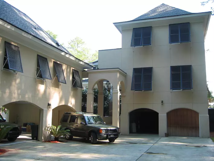 The front porch of a large home that has colonial shutters mounted beside all its windows.