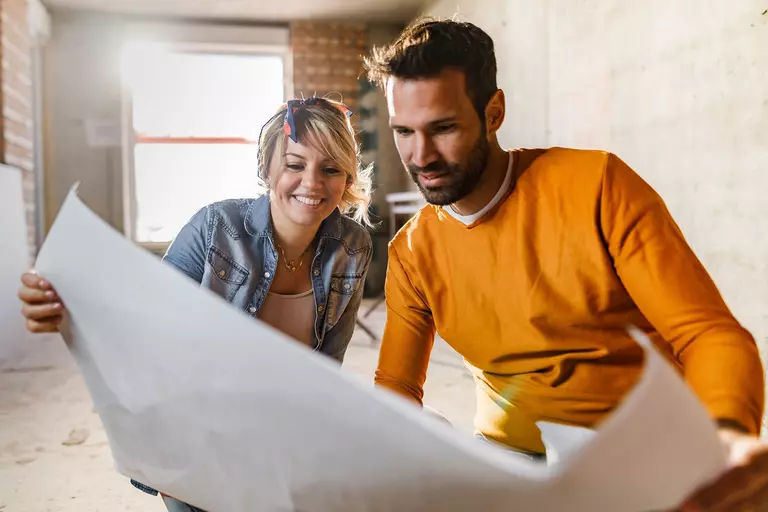 Young happy couple analyzing blueprints while planning a home remodel.