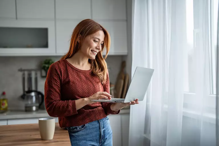 Woman standing up while holding her laptop with a smile on her face.