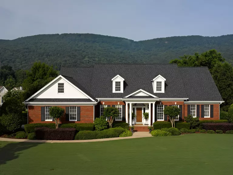 Front yard of a home with wooded mountains in the background.
