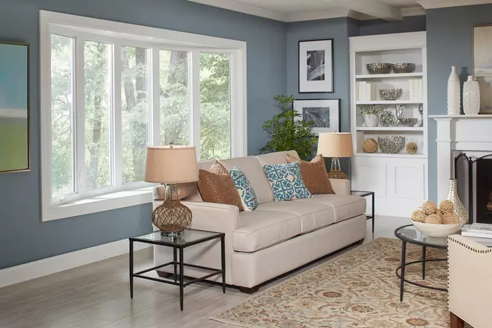 A picture containing bow windows in a living room with a couch, lamp, and other home décor. 