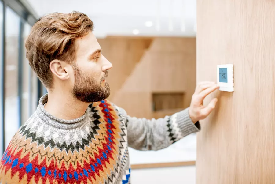 A man in a sweater checks living room temperature on a programmable thermostat