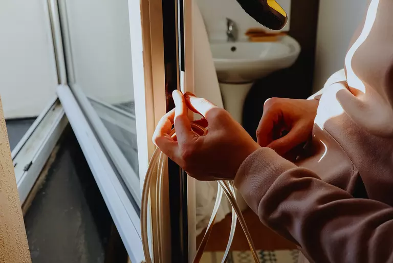 Person adding weatherstripping around the edges of a window.