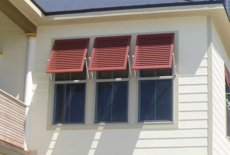 Three red-brown Bahama shutters that are open on their hinges at the top.