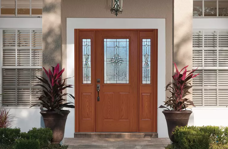 Front entrance of a home featuring a brown door with sidelites and matching large potted plants.