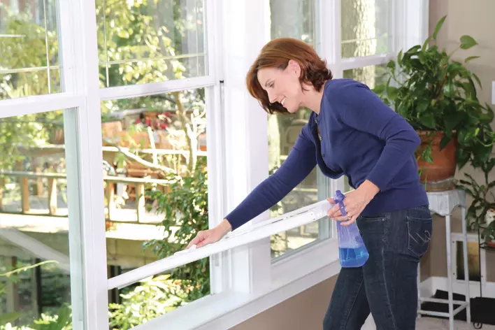 A woman removing the lower sash of a double-hung window and cleaning it while trying to figure out how to fix a window that won’t stay up.