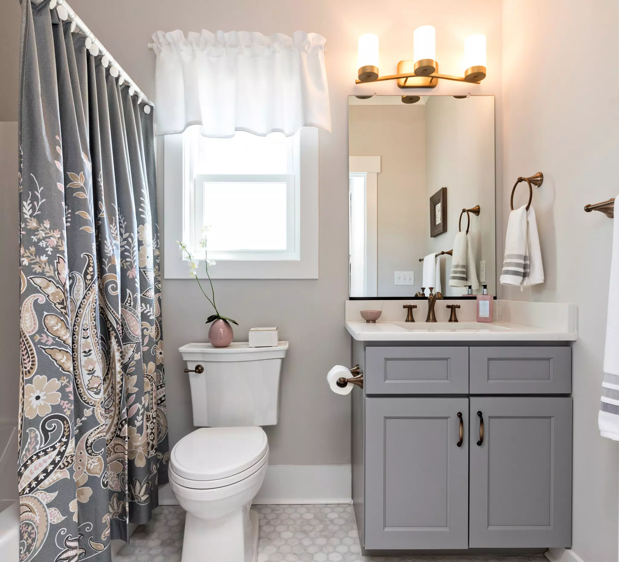 A gray updated sink vanity in a small bathroom with a bathroom window above the toilet