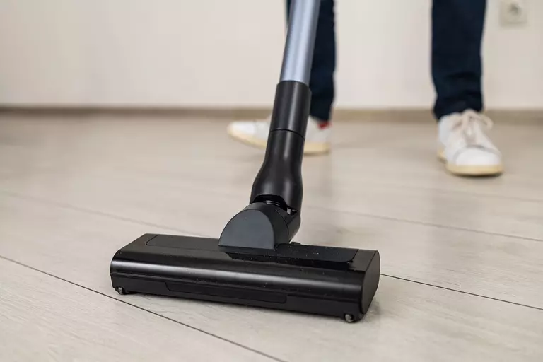 Compact black vacuum rolling over plank flooring.