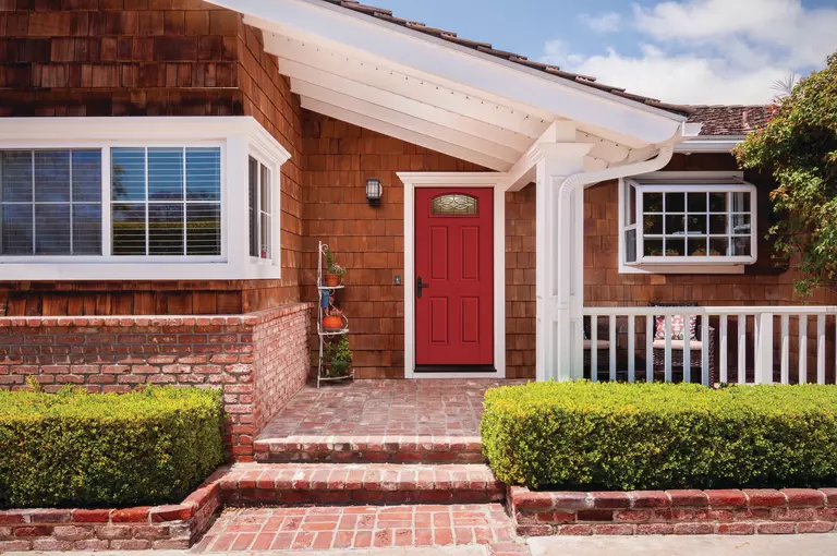 The outside of a home’s front porch featuring brick, wood shakes, and a red front door.