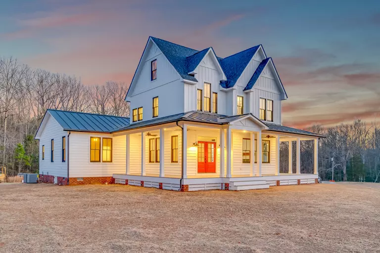 Whole view of a home with a wraparound porch and white siding.