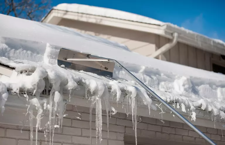 A roof rake being used for snow and ice removal on the roof of a home.