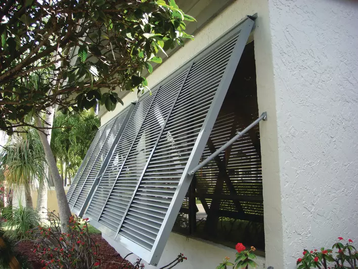 A home equipped with metal hurricane shutters over broad bay windows.