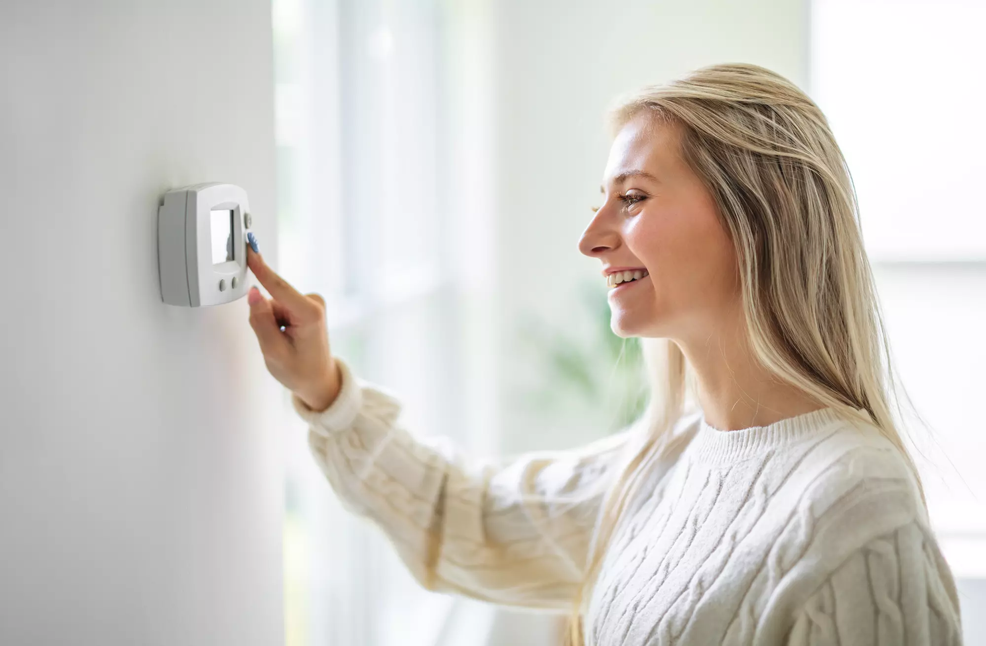 Woman smiling and adjusting a thermostat.