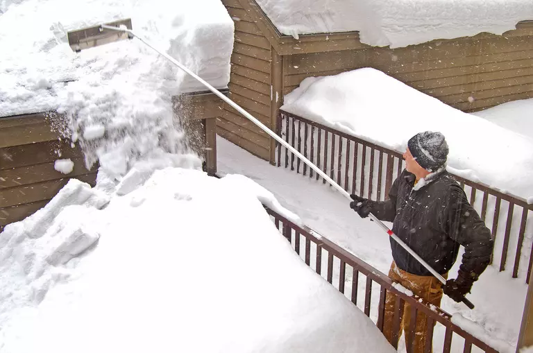 A man using a roof rake to remove snow from his roof that is heavy and could cause roof
damage.