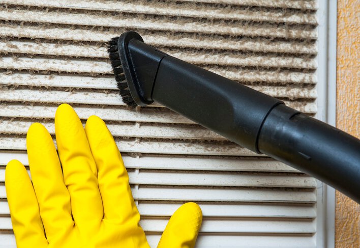 Person with yellow glove pressed up against HVAC system filter as they clean it with a vacuum brush.