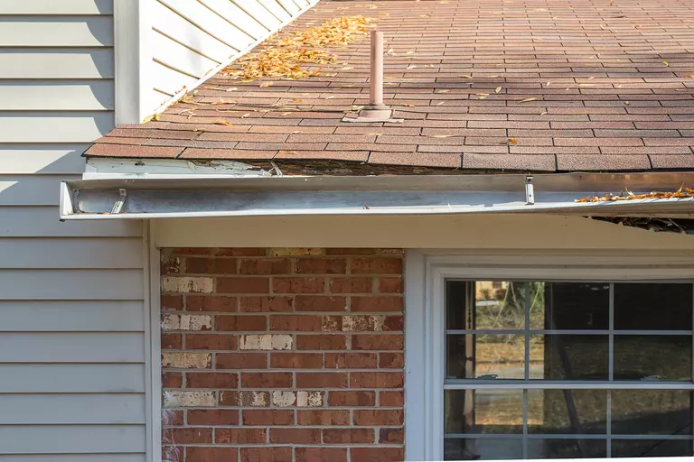 A warped, tilted section of gutters above the brick side of a house.