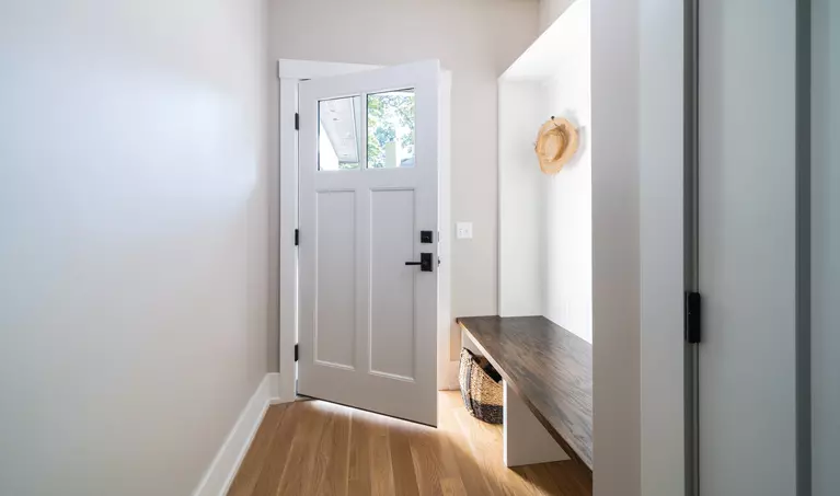 A white front door seen from the interior that’s opened partially with a pair of glass windows.