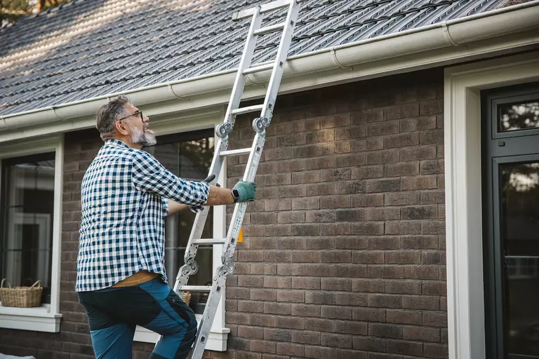 A contractor propping a ladder up against the gutters of a brick home as he prepares to clean the debris out of the gutters.