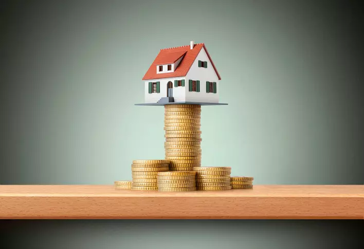 A model house atop a stack of coins meant to illustrate the financial investments of home ownership and DIY home renovations.
