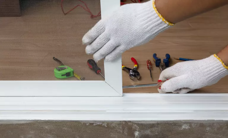 Pair of gloved hands and an assortment of tools working on a screened patio door.