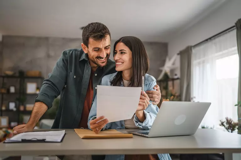A man and woman smiling while looking at a paper.