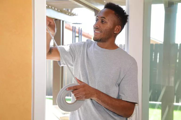 A man applies a roll of weatherstripping to the interior frame of a sliding door.