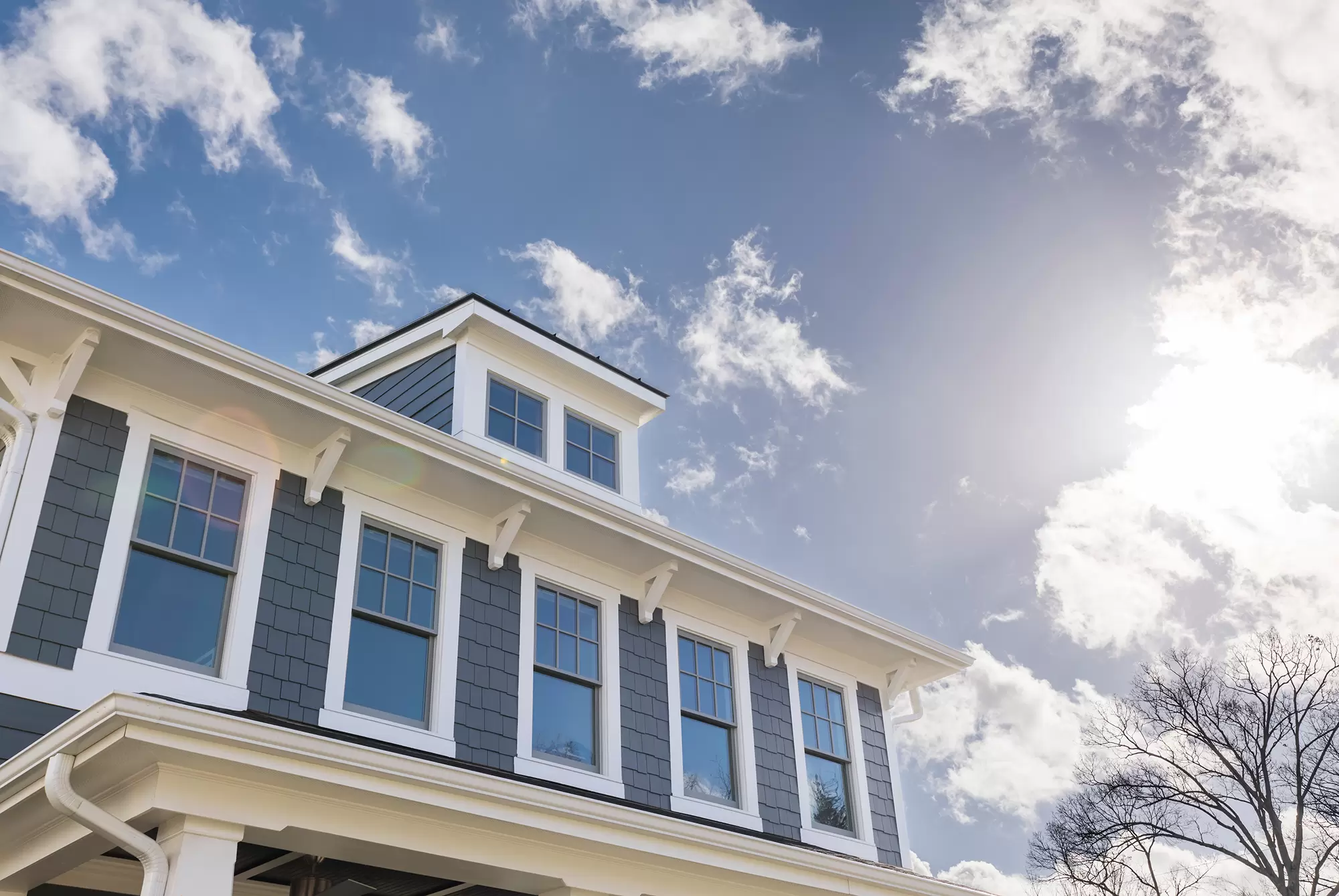 Upper level of a residential home with blue siding and double-hung windows with grids.